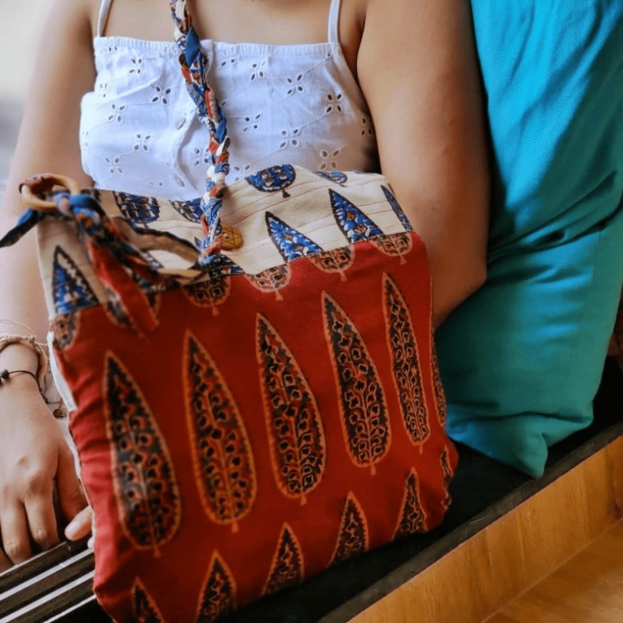 Woman sitting by the window with a sustainable hand block printed maroon and off-white cotton sling bag with braided strap